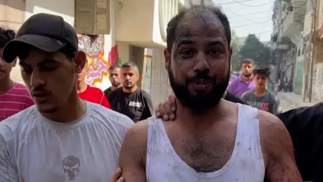 A man crying walking through the streets, surrounded by other men