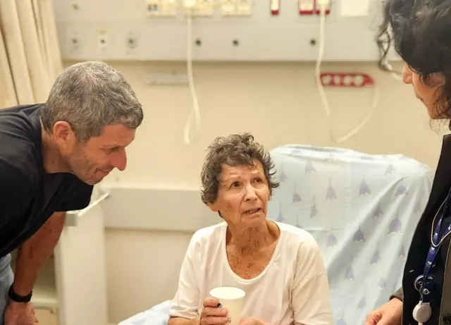 Yocheved Lifshcitz talking to two people, sitting in a hospital bed