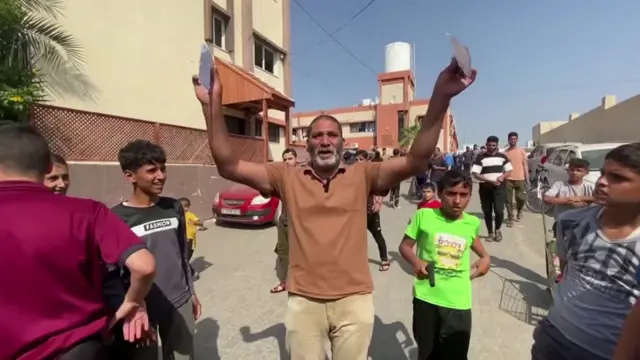 A man surrounded by children. He holds leaflets in the air