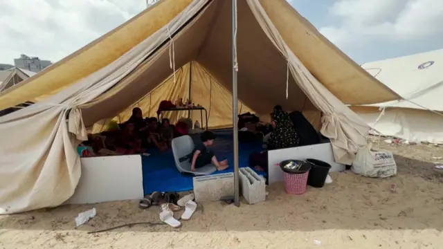 A tent with the front open. Families sit inside, a young child sits at the front