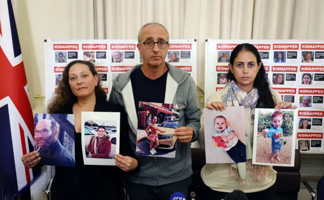 (L-R) Ayelet Svatitzky, David Barr and Ofri Bibas Levi, relatives of Israeli hostages, hold photographs of loved ones and murdered Hamas victims during a press conference at the Israeli Embassy in London