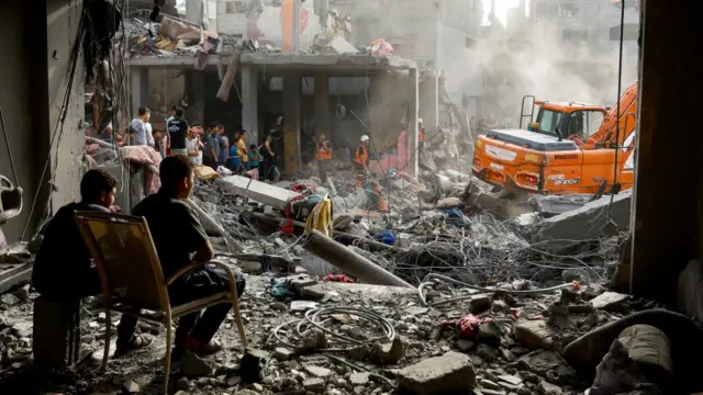 Two teenage boys watch on as emergency service personnel pick through the rubble for casualties after Israeli strikes on Khan Younis