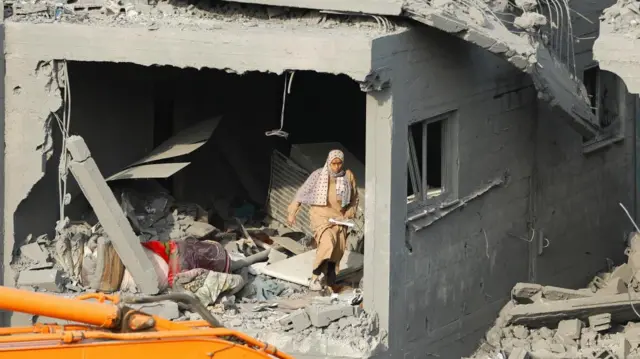 A Palestinian woman walks amid the rubble in the aftermath of strikes