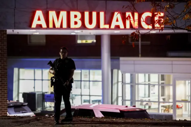 A police officer stands guard in front of the Central Maine Medical Center after a man reportedly opened fire killing and injuring numerous people in Lewiston, Maine, USA