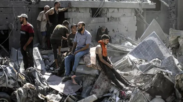 Men sit on rubble in Khan Younis