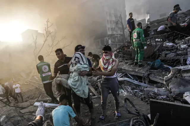 A Palestinian man carries a wounded woman after recovering her from the rubble of a destroyed area following Israeli air strikes in Gaza City