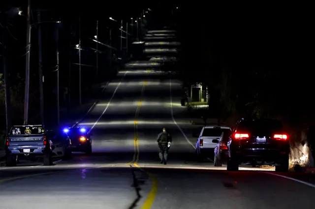 A law enforcement officer walks along the road leading to the Schemengees bar where a man reportedly opened fire earlier this evening killing and injuring numerous people in Lewiston, Maine