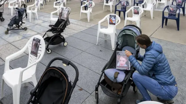 A person sticks a photo of a young child to a pram parked among chairs and other prams