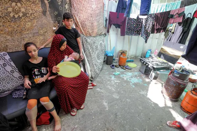 A woman sits alongside two children as she holds her baby outside the Al Shifa hospital