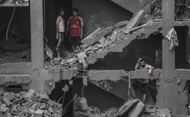 Three men walk around a heavily damaged building in the Gaza Strip