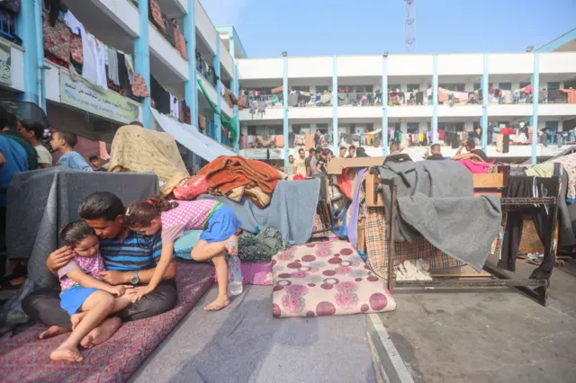 A Palestinian family sit in the playground of a school run by the United Nations Relief and Works Agency for Palestine Refugees (UNRWA) agency that has been converted into a shelter for displaced Palestinians in Khan Yunis in the southern Gaza Strip.