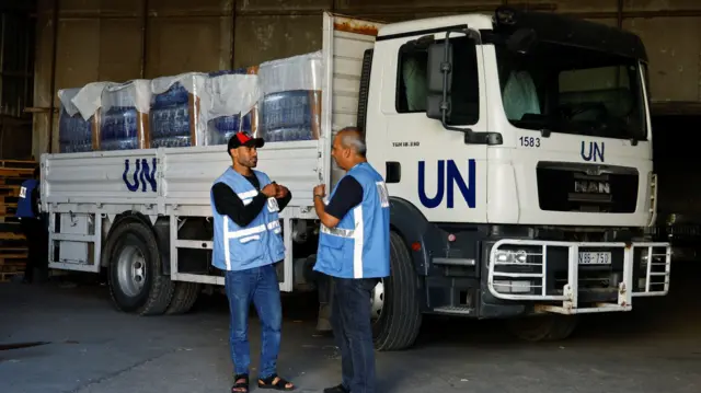 Workers stand by a United Nations vehicle, while sorting aid to be distributed to Palestinians,