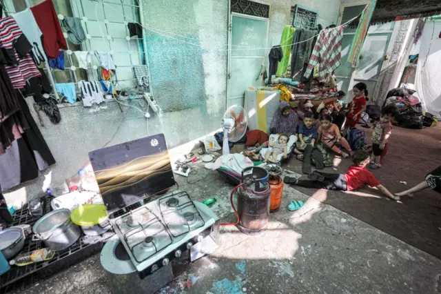 Women and children shelter outside Al Shifa hospital. A stove with a gas cannister attached can be seen in the foreground, with washing hanging up on the wall