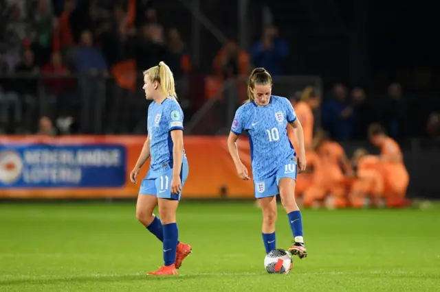 Hemp and Toone stand with the ball at the centre circle as Netherlands celebrate in the background.