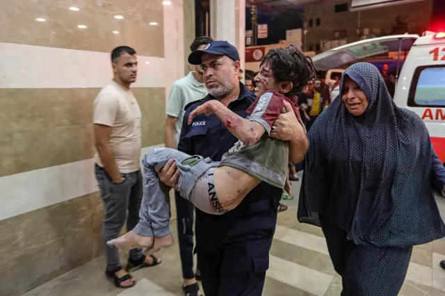 A policeman carries a wounded child into Nasser Medical Hospital