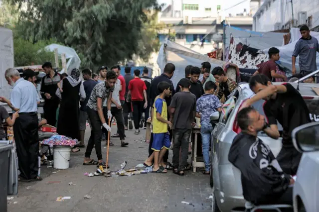 A man sweeps rubbish outside Al Shifa hospital, with lots of others crowded round