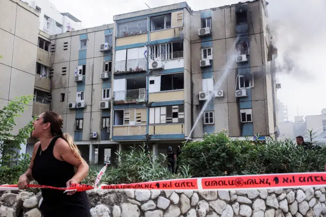 A woman calls out as smoke rises from a residential apartment building, with tape cordoning the area