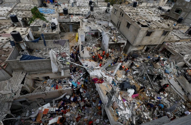 Emergency personnel and people check the damage at the site of Israeli strikes on houses, amid the ongoing conflict between Israel and Palestinian Islamist group Hamas, in Khan Younis