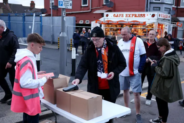 A Luton Town fan buys a match day programme outside the stadium