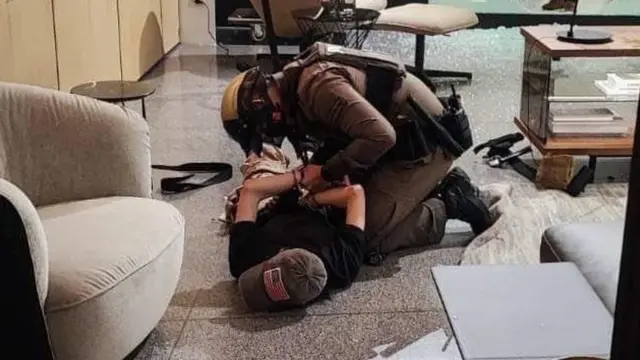 A police officer pins a teenager, who is wearing a cap, to the ground