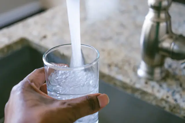 Close-up of unrecognizable black woman filling glass with water from kitchen sink