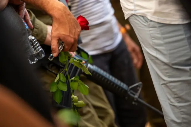 A person holds a flower near a soldier carrying a rifle during the funeral of Lili Itamari, 63, and Ram Itamari, 56,