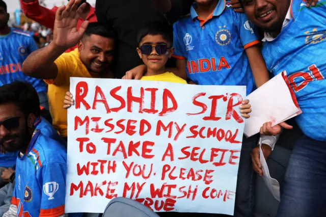 A spectator holds a sign up asking Rashid Khan for a selfie