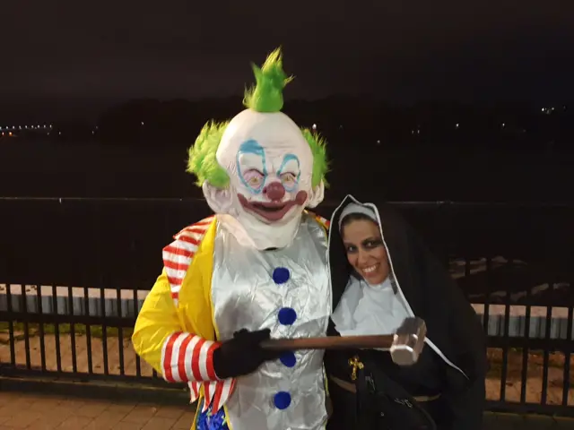 Shows Mike dressed as a clown with a large hammer in his hand and Lalya dressed as a nun