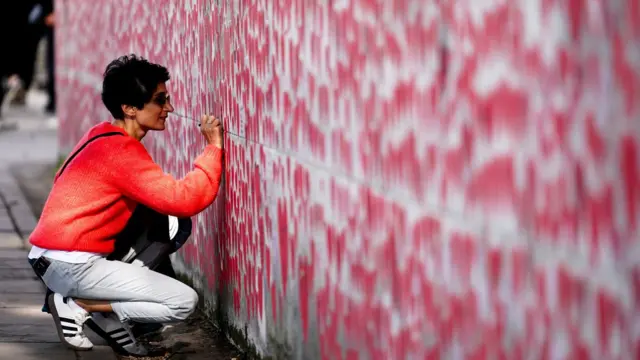 Woman writing on a wall which is covered in red hearts