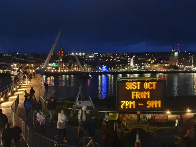 Night scene of people crossing Derry's Peace Bridge