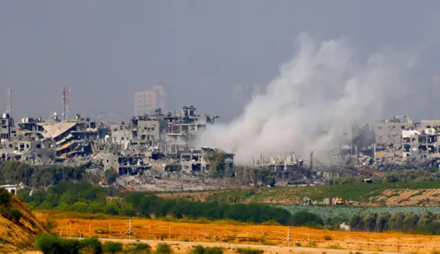 A bombed out neighbourhood in Gaza, smoke from recent attacks is rising over the heavily damaged buildings.