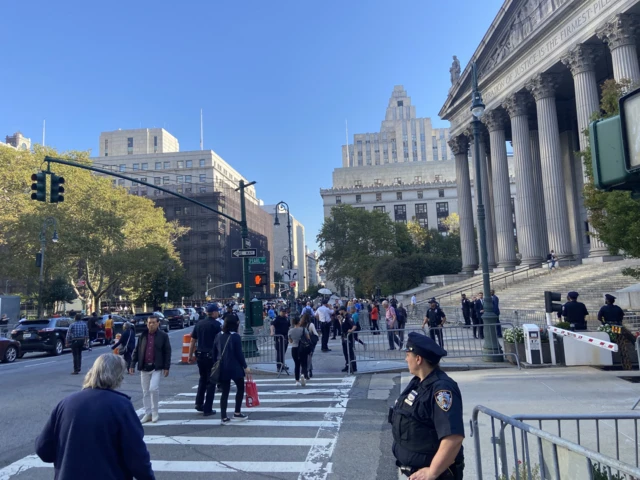 Columns and steps of courthouse, traffic signal, people crossing street, police officer and barricade