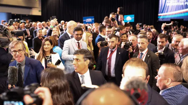 Sunak pictured among a crowd of members of the media and others after his speech at the party conference