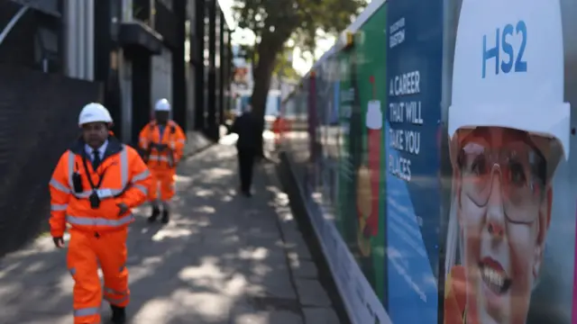 Workers walk beside a HS2 sign