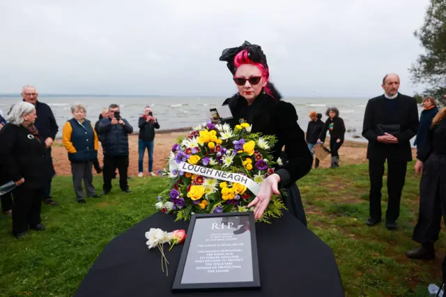 An environmental campaigner places a floral wreath on a coffin signifying Lough Neagh at a "wake" for the lake in September