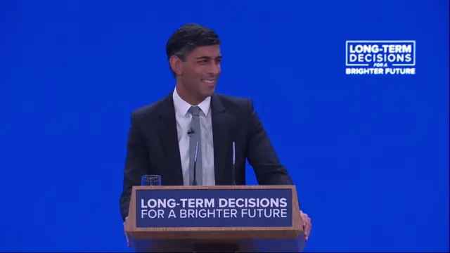 Rishi Sunak smiles as he addresses conference