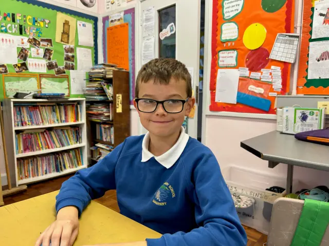 Jack, a schoolboy in a library, wearing school uniform and glasses