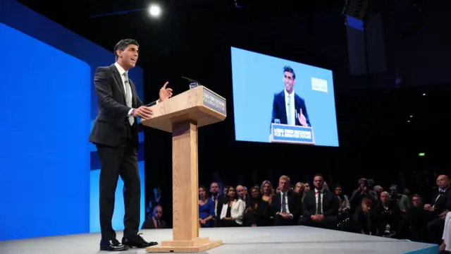 Rishi Sunak on stage with a screen of him in the background