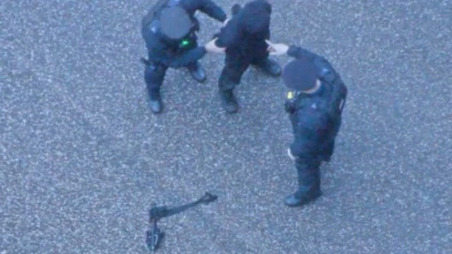 Chail being arrested by two police officers, with the crossbow on the ground nearby