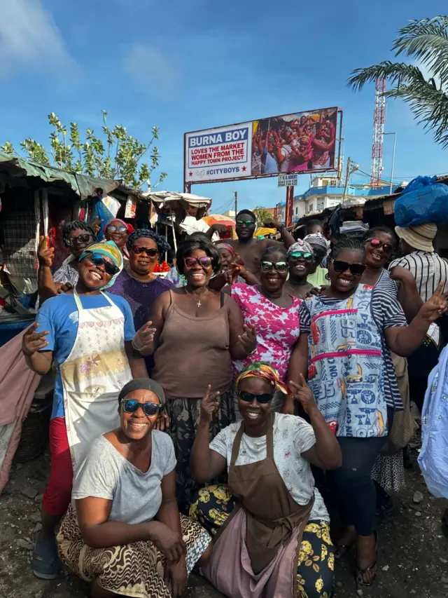 Nettey and the ladies of Makola market infront of the billboard from Burna Boy