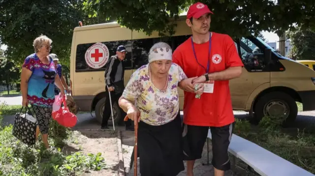 A Red Cross volunteer helps an elderly woman to evacuate from the city of Kupiansk-Vuzlovyi in Kharkiv region, amid Russia's attack on Ukraine, in Kharkiv, Ukraine August 15