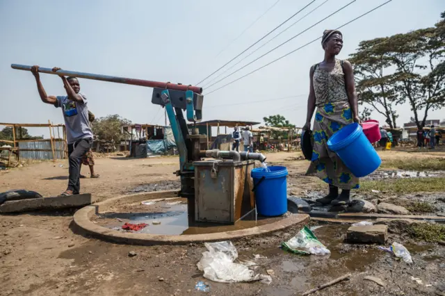 A young boy pumps water from a borehole as a woman collects water into buckets in Glen View, a suburb of Zimbabwe's capital Harare where the cholera outbreak was first detected, on September 19, 2018.