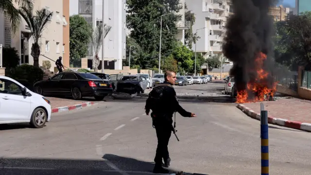 A member of Israel's police forces walks towards a fire as rockets are launched from the Gaza Strip, in Ashkelon