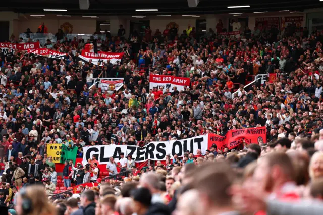 A banner reading 'Glazers Out' is draped across the corner of Old Trafford above the tunnel.