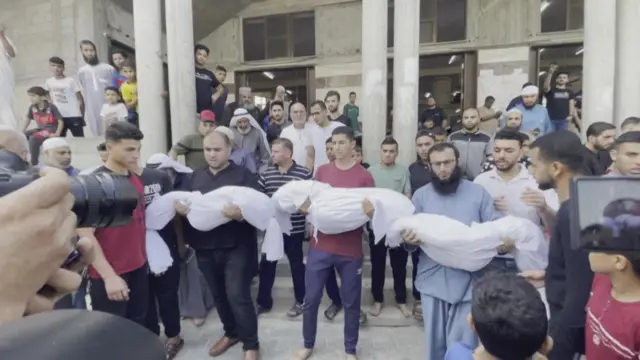 Three men hold three bodies wrapped in white linen and pose for a photo during a funeral procession in Rafah, in the southern Gaza Strip