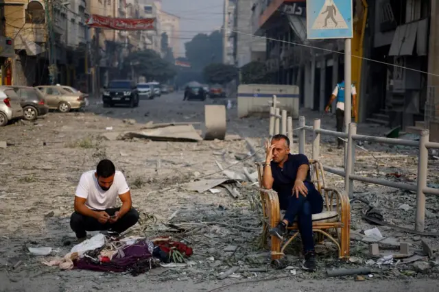 Residents sit on a debris-strewn street near the Watan Tower