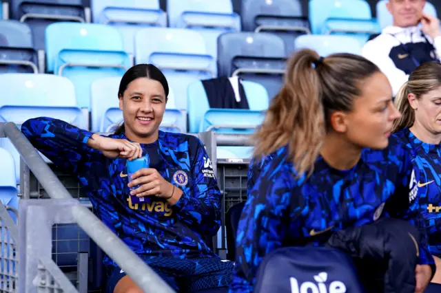 Sam Kerr holds a water bottle while sitting on the bench.