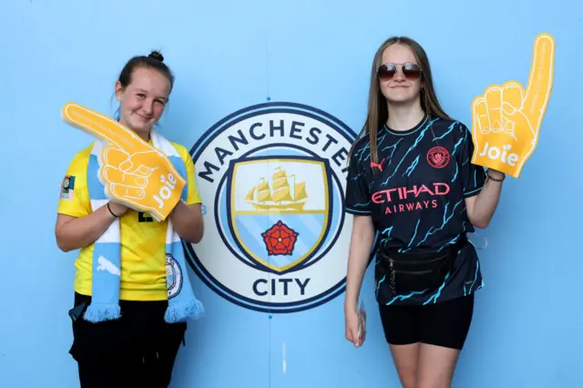 City fans pose with foam fingers in front of the club badge at the stadium.