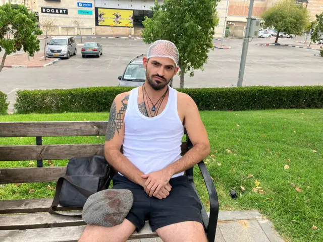 Gilad sitting on a bench with his bloodied hat on his lap