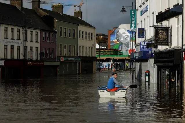 A man sits in a boat in water as it flows through streets after heavy rain caused extensive flooding, ahead of the arrival of Storm Ciaran, in the city centre of Newry, Northern Ireland,